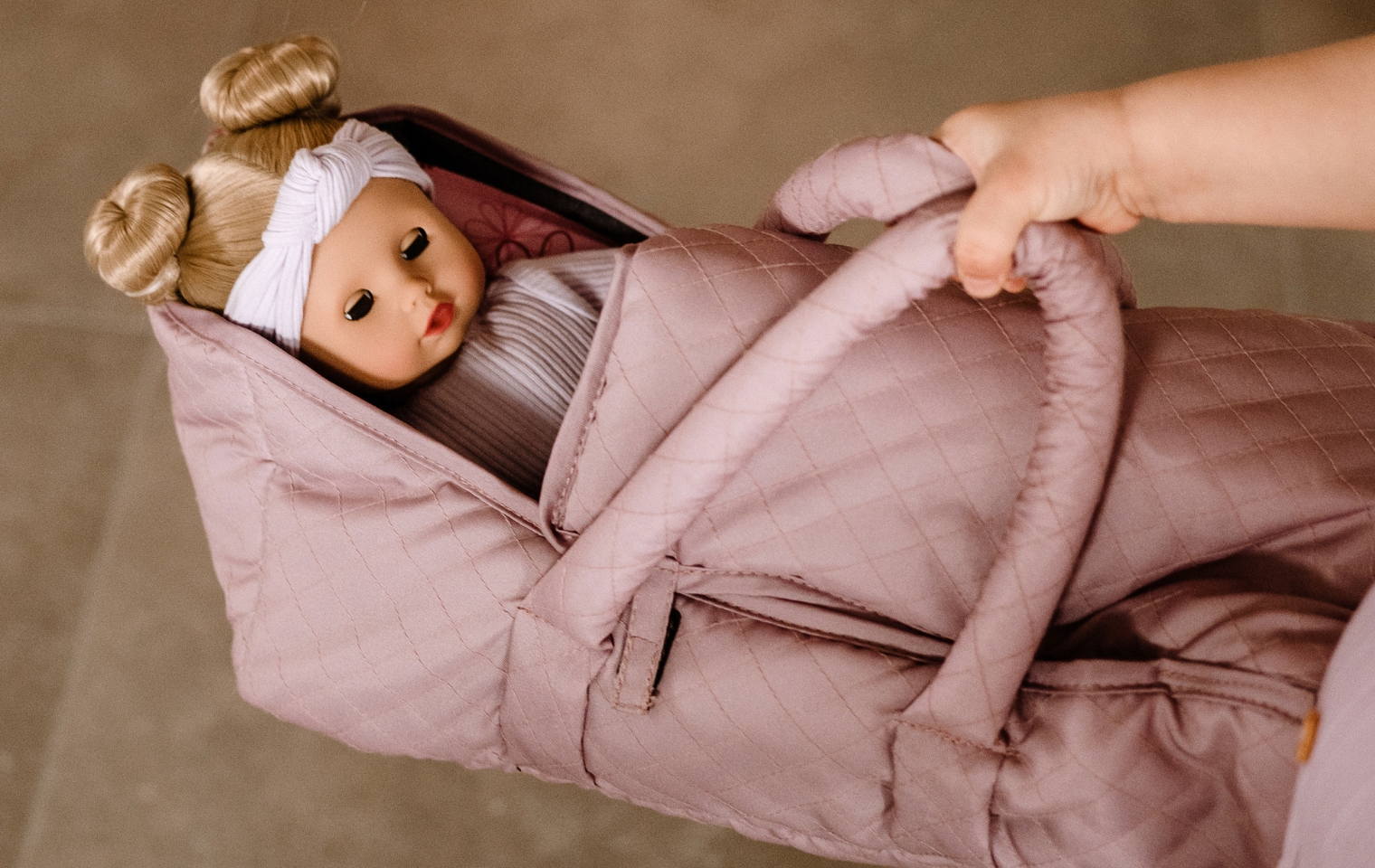 Reisen mit Kindern Goetz Kind traegt eine rosa Puppentrage mit einer Babypuppe mit blonden Haaren und Schlafaugen in der Hand