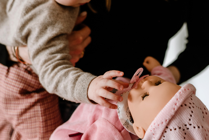 Kind gibt einer Babypuppe den Schnuller