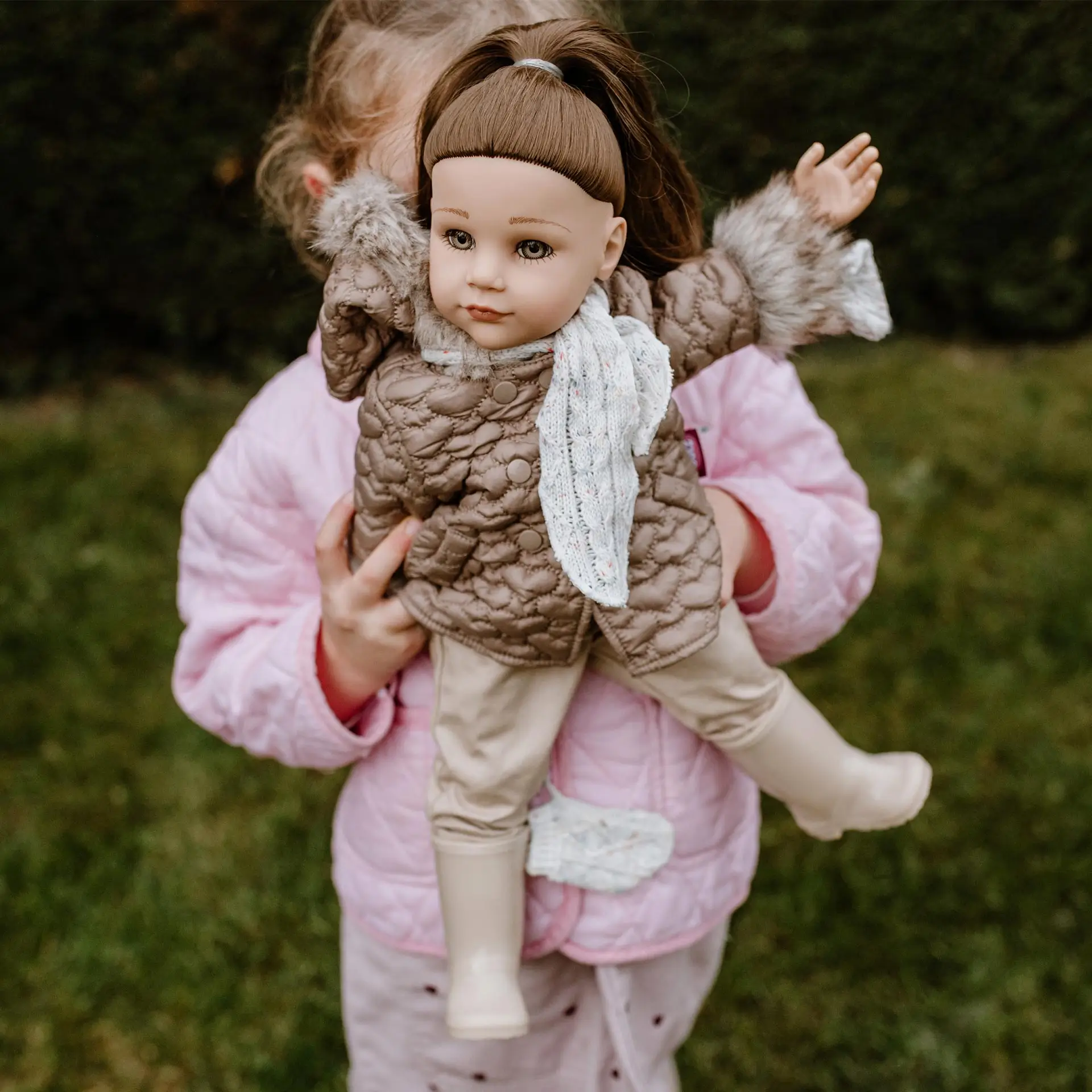 Kind haelt 50 cm grosse Stehpuppe mit braunen Haaren, die ein Winteroutfit traegt, im Arm