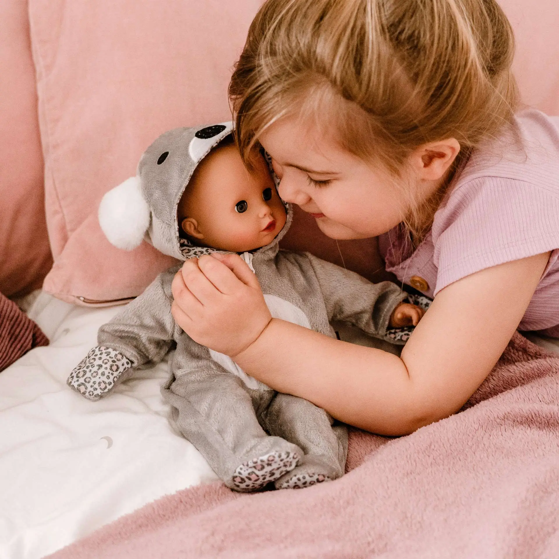 Kind kuschelt mit einer 33 cm großen Babypuppe im Koala-Onesie