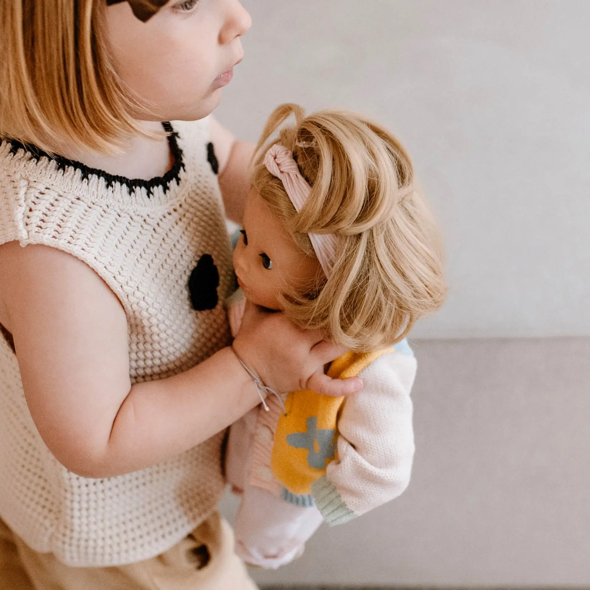 Kind haelt 33 cm große Babypuppe mit blonden Haaren im Arm