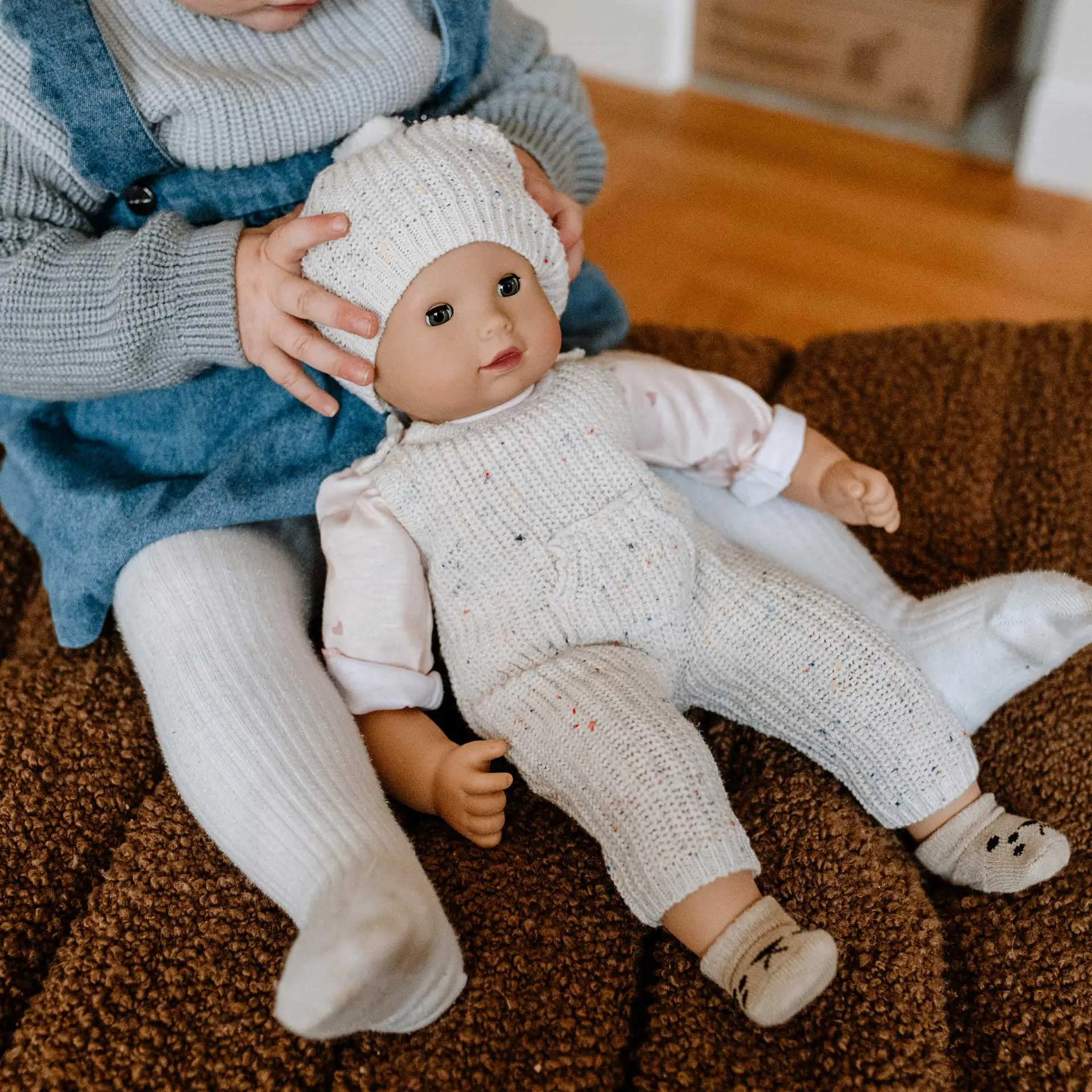 Kind spielt mit 42 cm grosser Babypuppe im beigemelierten Strickanzug und passender Strickmuetze