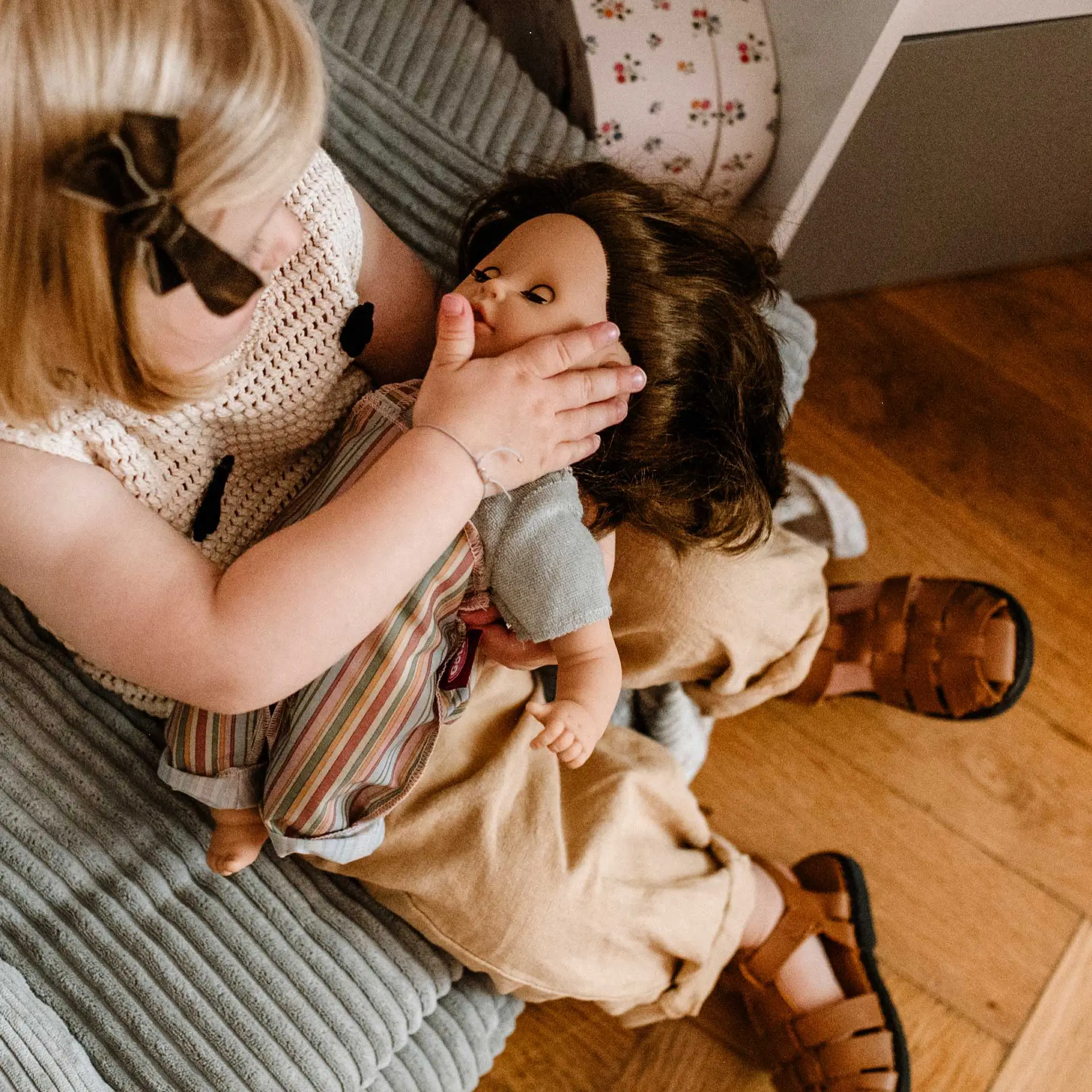 Kind haelt eine 33 cm große braunhaarige Babypuppe mit Schlafaugen in den Armen
