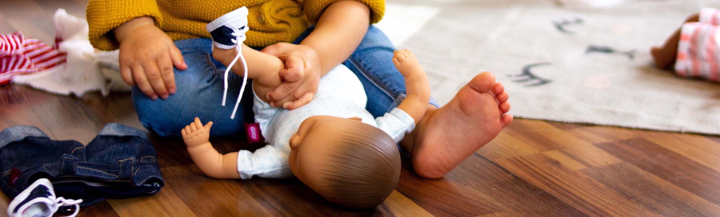 Kind spielt mit Götz Puppe und zieht ihr Puppenklamotten von Götz an 