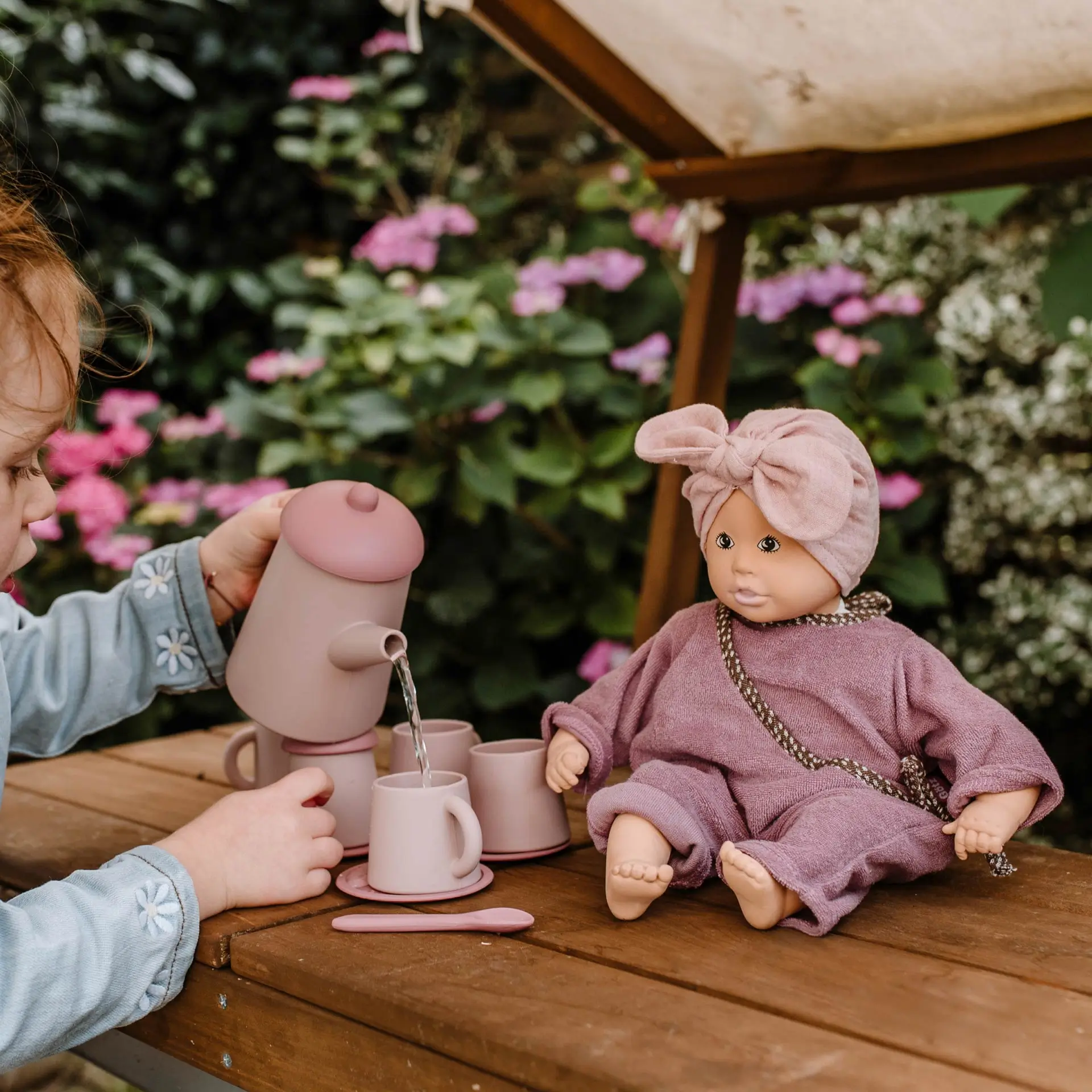 3403562 2333013 Teeset und Baby Pure Cosy Lina Goetz Kind spielt im Garten mit 33 cm großer Babypuppe im rosa Outfit und gießt Wasser in eine Teetasse ein