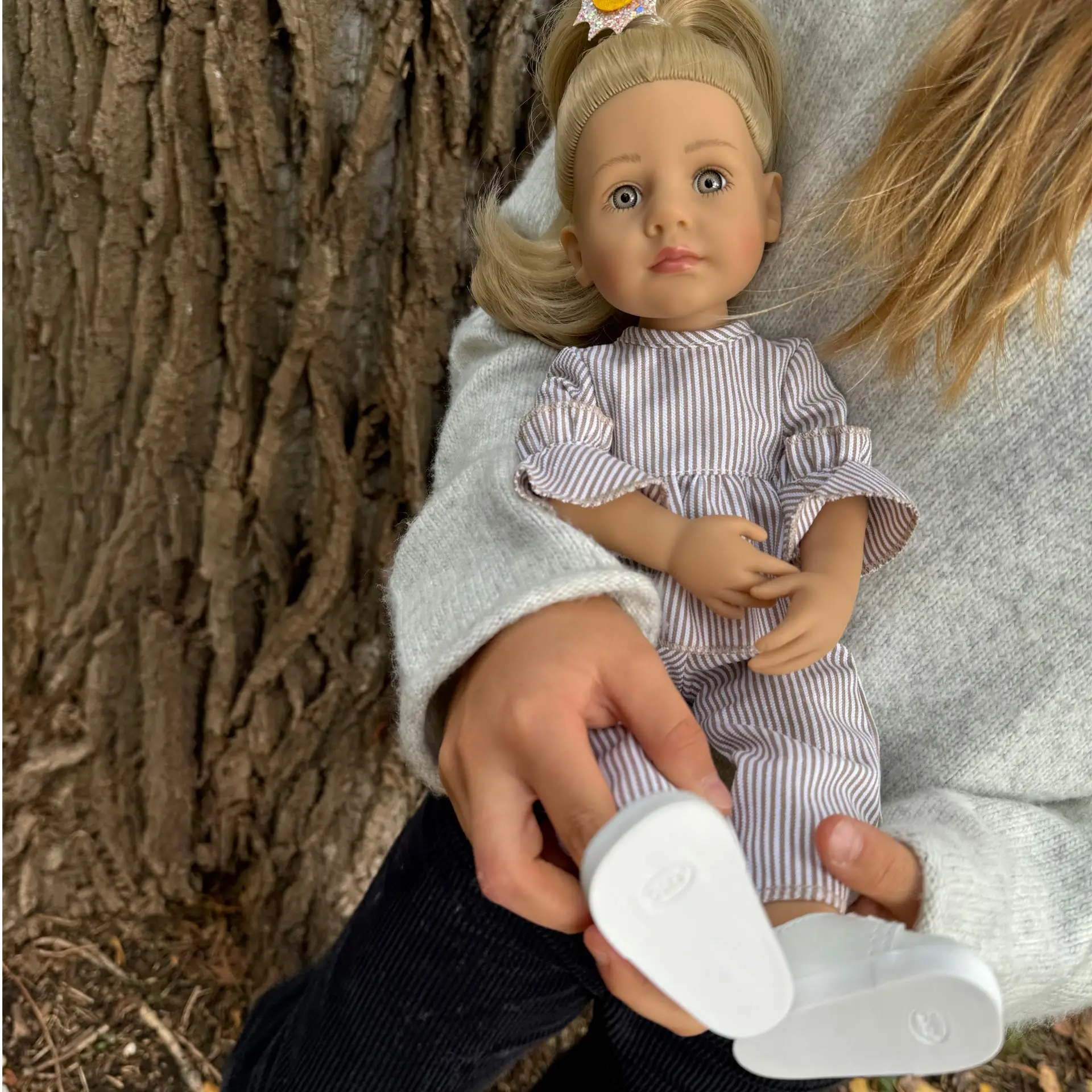 Kind haelt eine 36 cm große Stehpuppe mit blonden Haaren blauen Augen und gestreiftem Zweiteiler im Arm