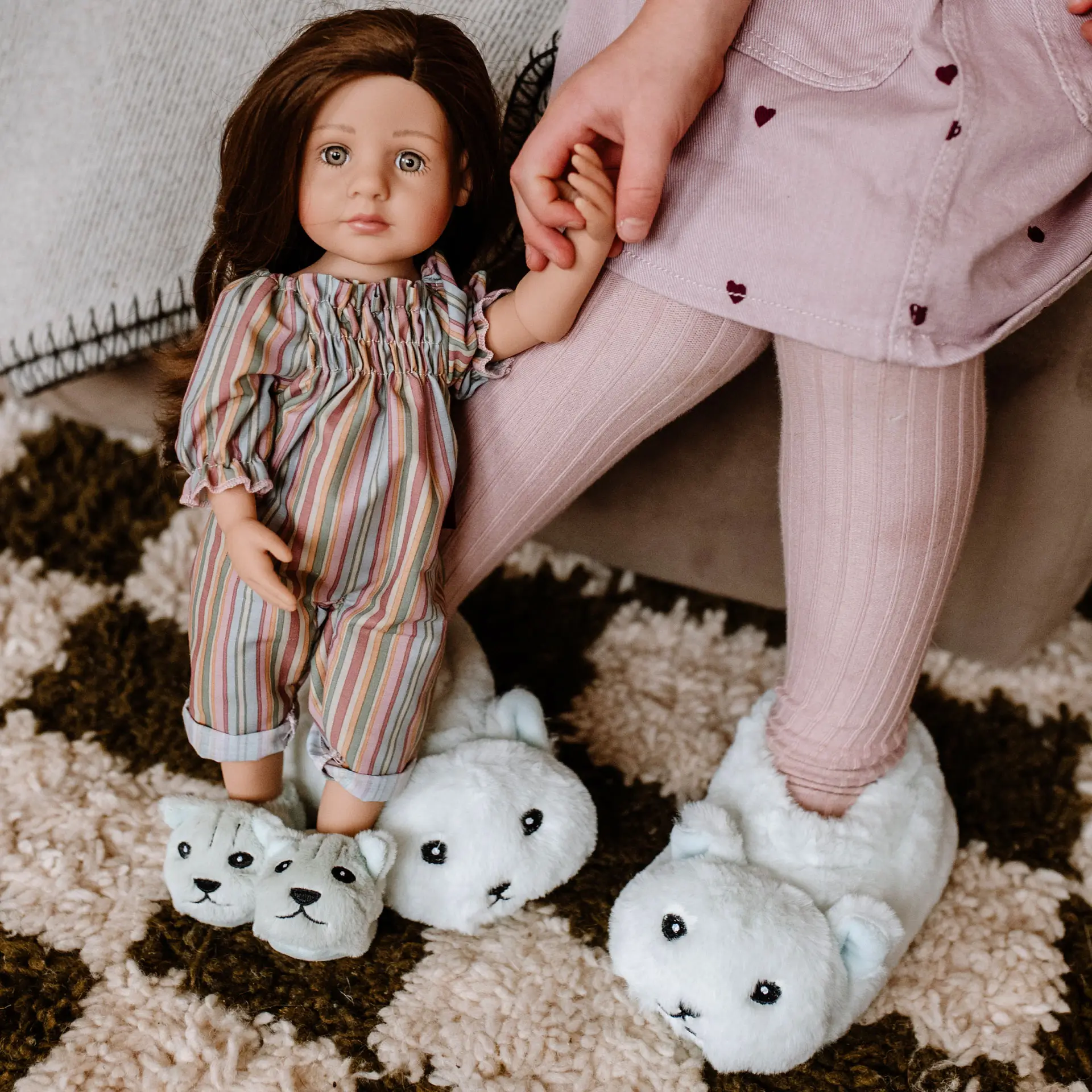 Kind spielt mit 36 cm grosser Stehpuppe mit braunen Haaren; beide tragen die gleichen Plueschhausschuhe im Partnerlook