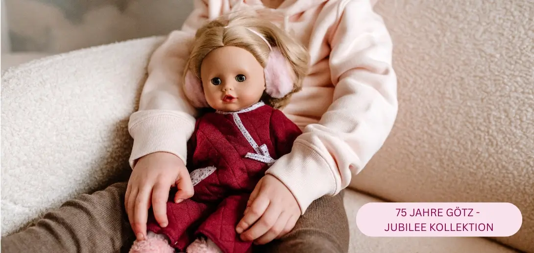 Kind spielt im Kinderzimmer mit 33 cm grosser Babypuppe mit Schlafaugen und blonden Haaren, gekleidet im bordeauxfarbenen Anzug