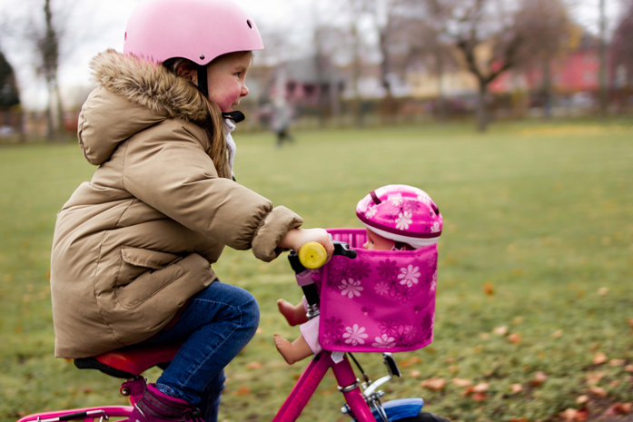 Kind und Puppe fahren gemeinsam Fahrrad