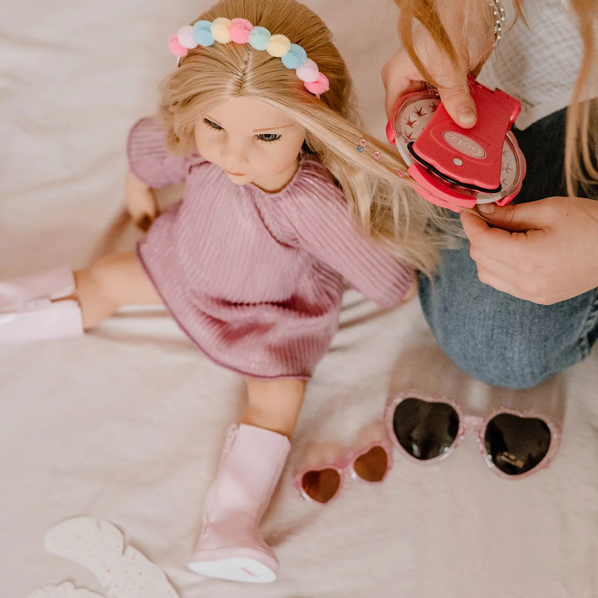 2159096 Hannah Be My Mini Me Goetz Kind bringt mit einem Glitzerapplikator Glitzersteinchen auf das Haar einer 50 cm grossen blonden Stehpuppe im rosa Kleid auf
