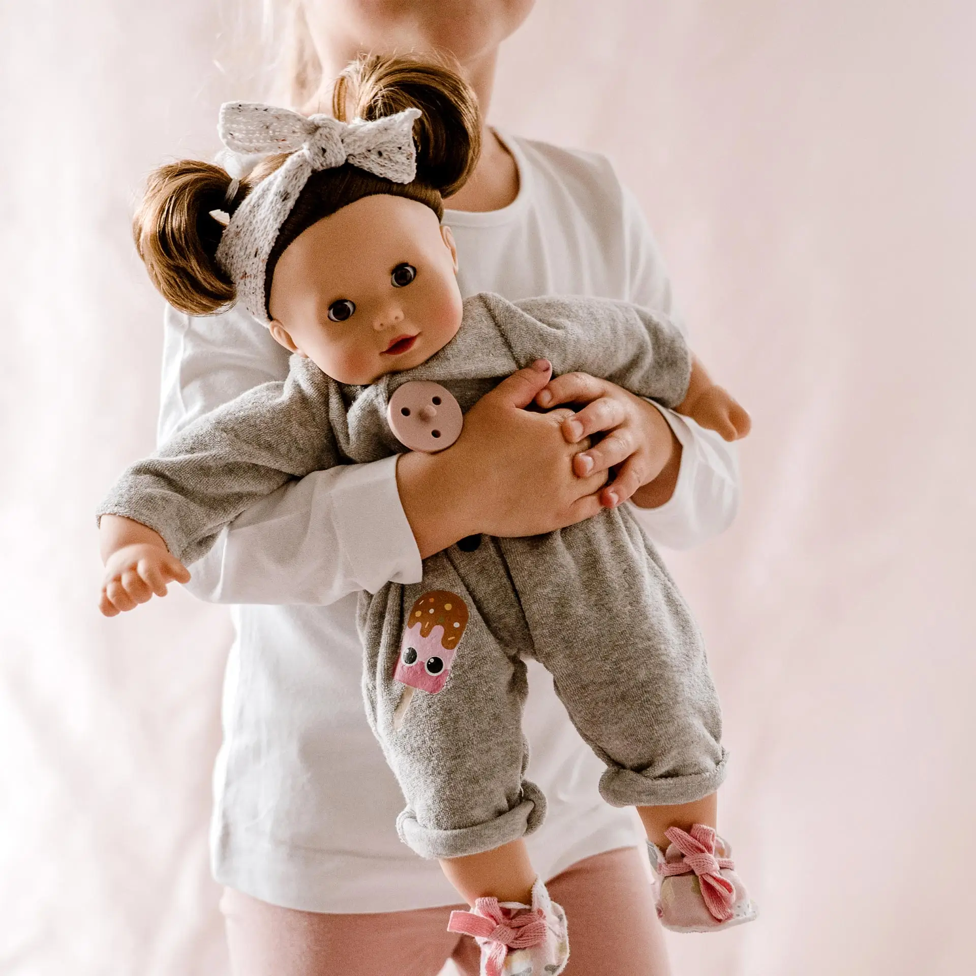 2327113 Maxy Muffin Popsicle Goetz Kind umarmt eine 42 cm große braunhaarige Babypuppe mit Schlafaugen und grauem Frotteanzug