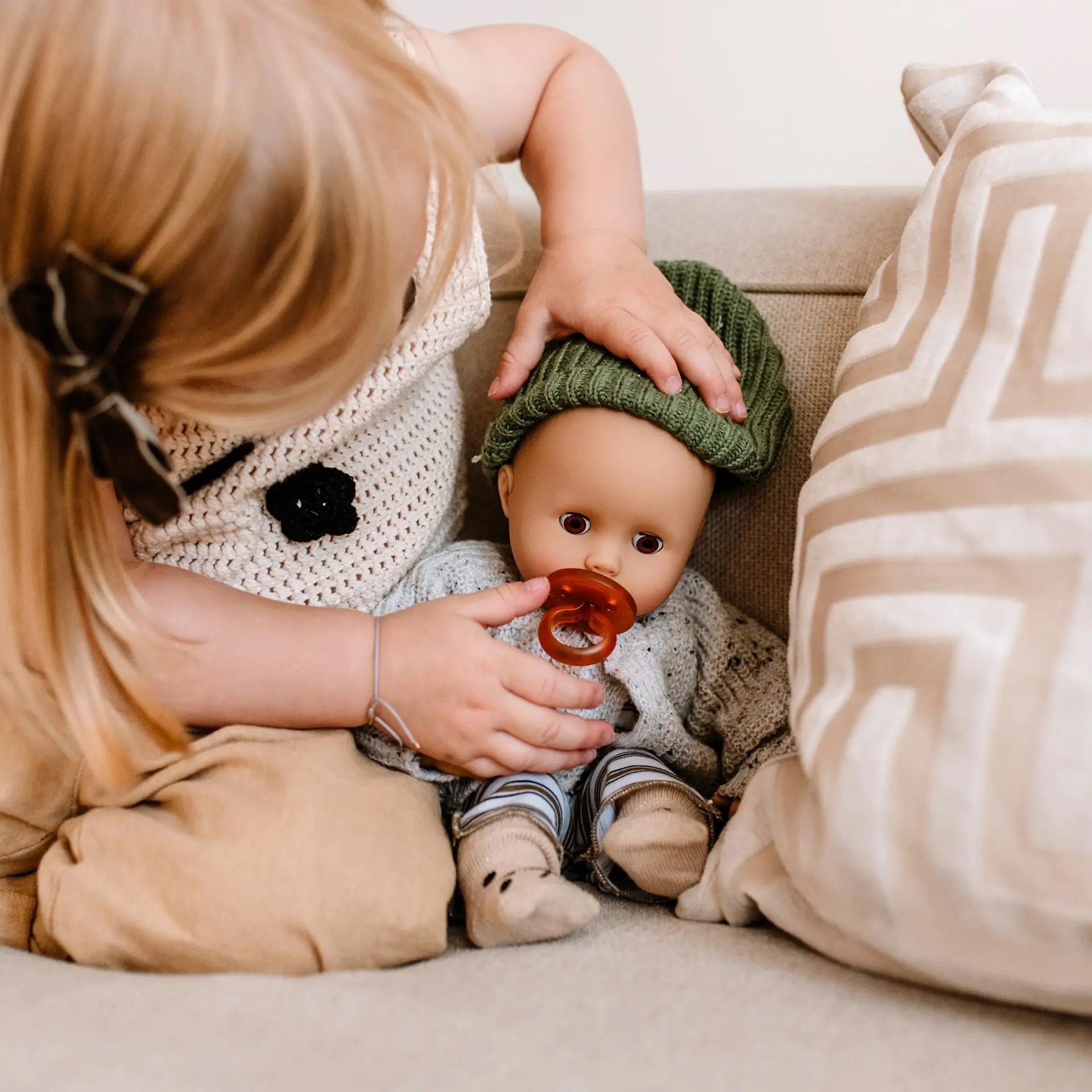 Kind gibt einer 33 cm großen Babypuppe mit Schlafaugen einen Schnuller