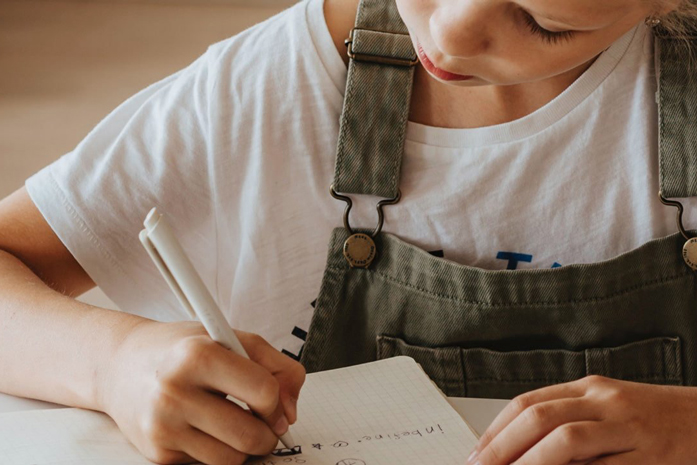 Kind schreibt auf ein Blatt Papiert mit einem Kugelschreiber