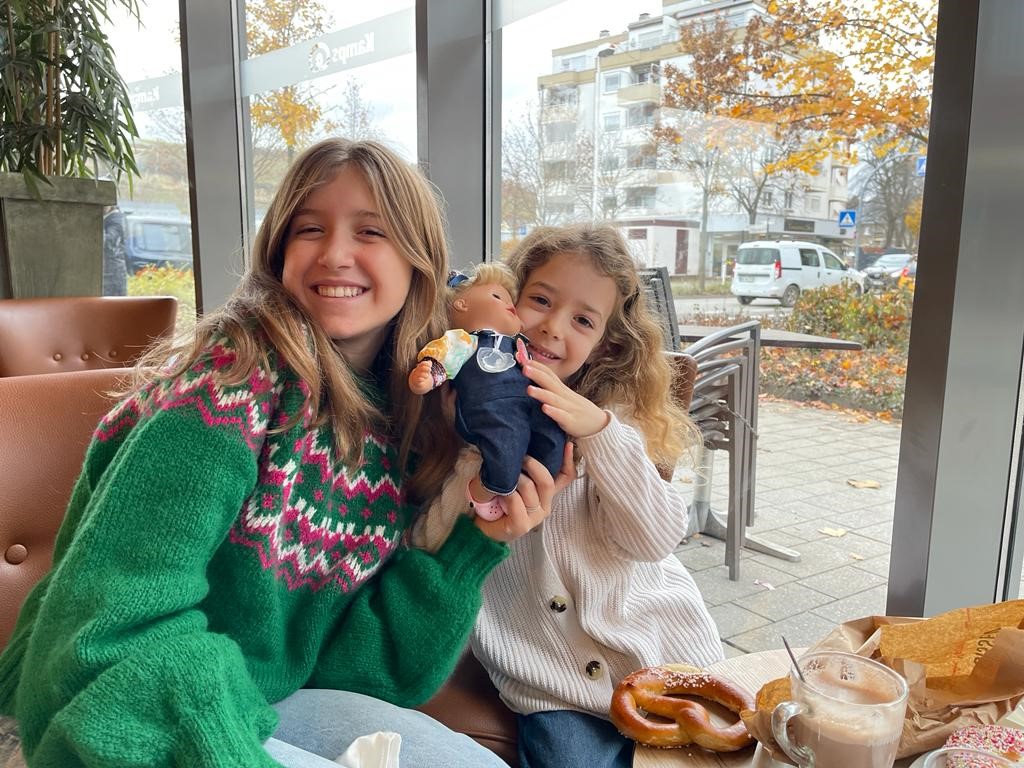 Zwei laechelnde Kinder halten gemeinsam eine 33 cm grosse Babypuppe in der Hand