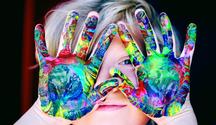 Kind hält bunte Hände vor dem Gesicht