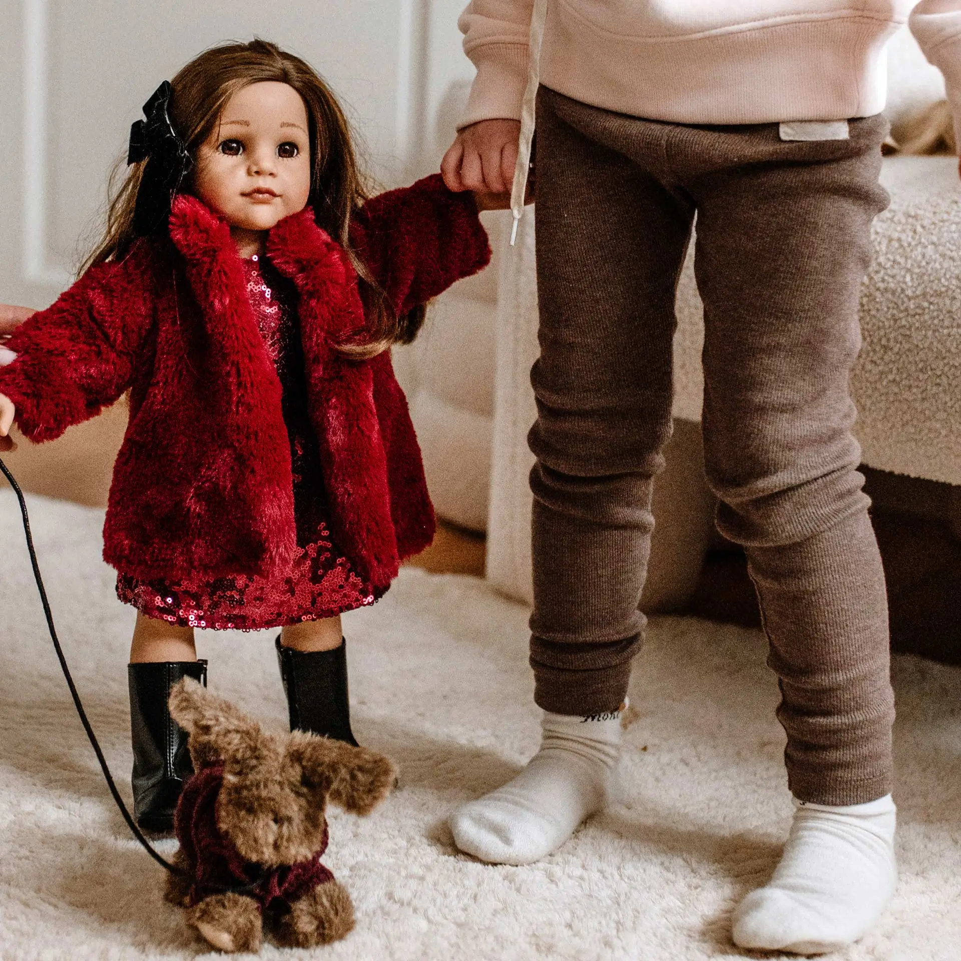 Kind haelt die Hand einer 50 cm grossen braunhaarigen Stehpuppe im roten Mantel mit Plueschhund