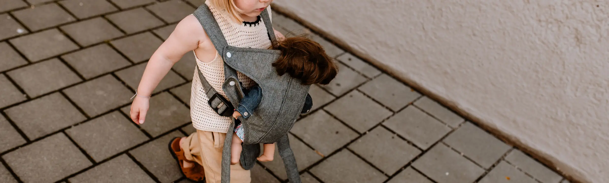 Kind traegt eine Babypuppe in eine  Bauchtrage