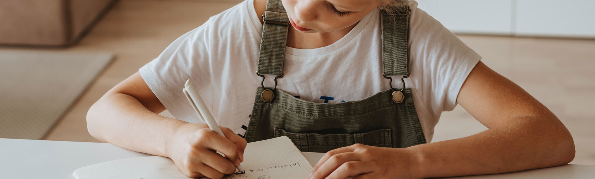 Kind schreibt an einem Tisch und bereitet sich auf den Schulstart vor mit den tipps von Götz