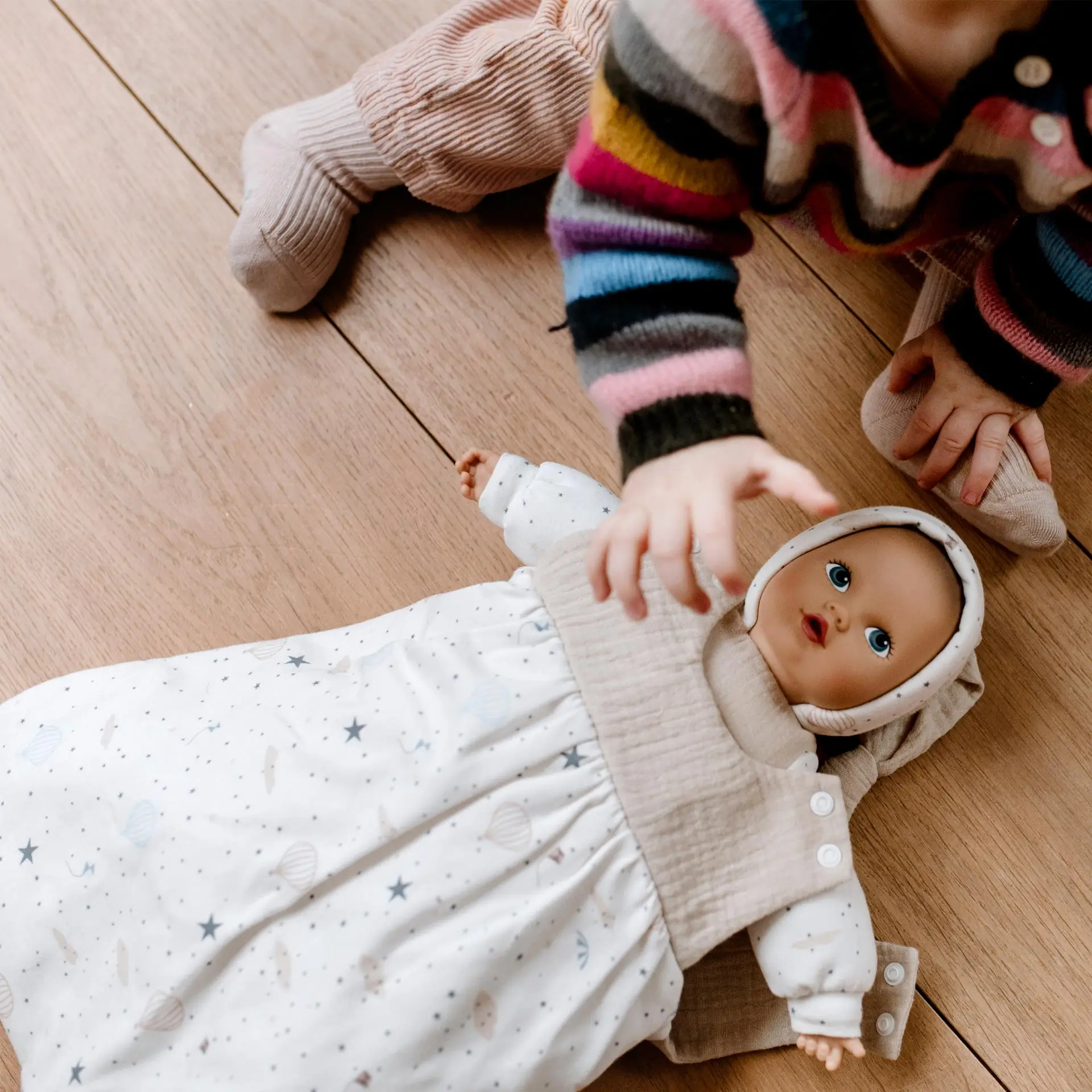 Kind spielt mit Erstlingspuppe in Schlafsack welcher mit Heißluftballons bedruckt  ist