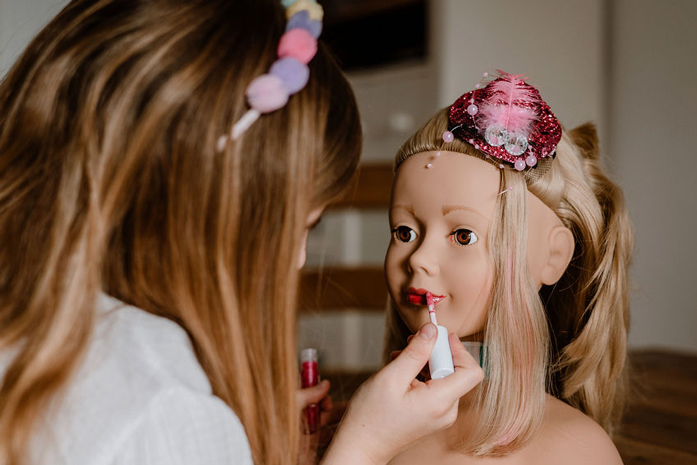 Kind schminkt blondem Frisierkopf die Lippen mit Lippenstift