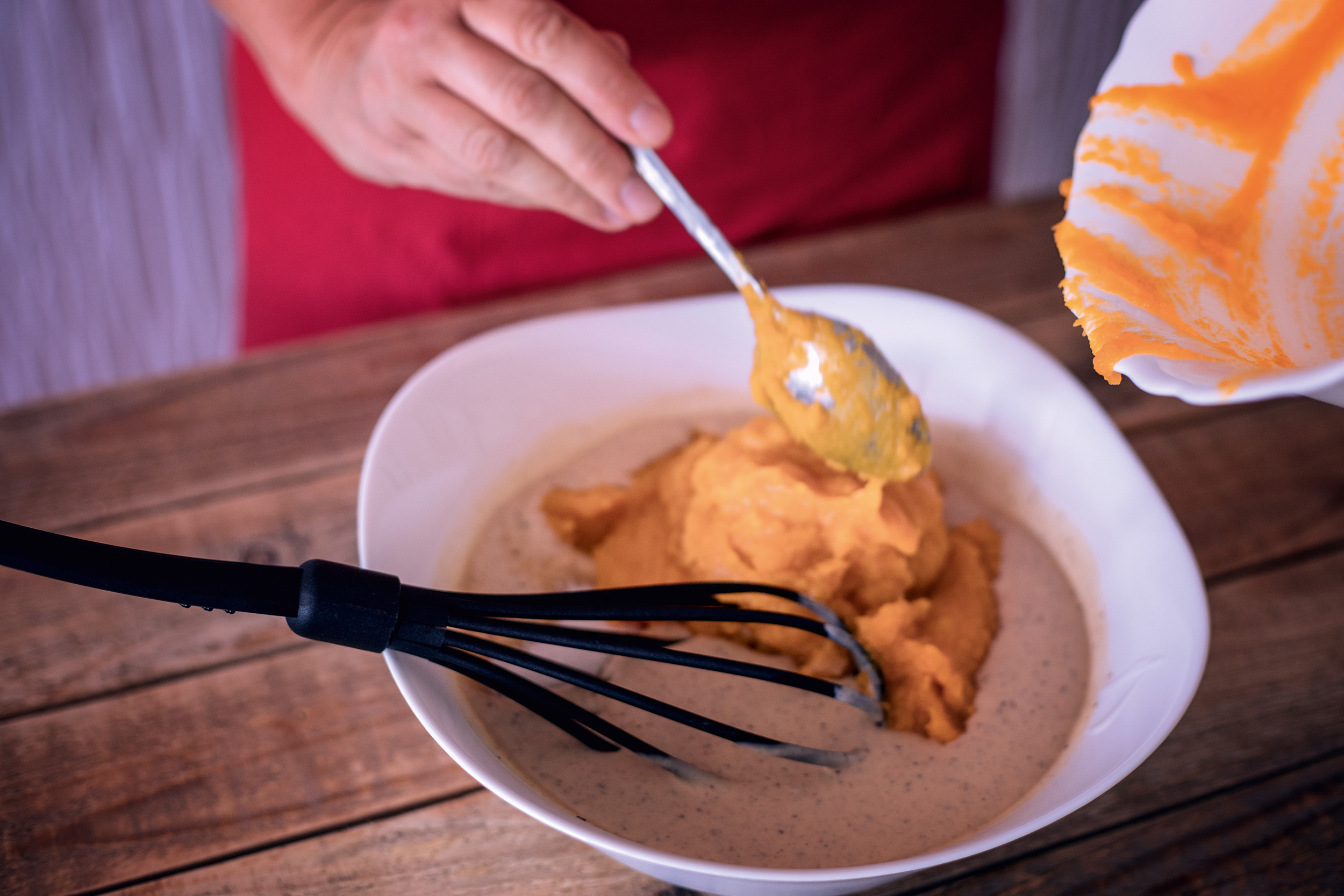 Kuerbispueree wird mit Schneebesen in Schuessel verruehrt