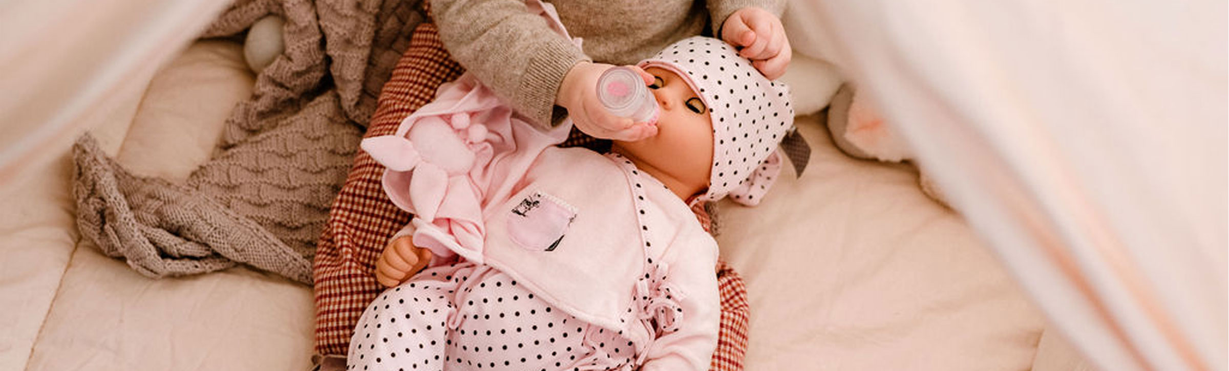 Kind fuettert 48 cm große Babypuppe mit Flasche