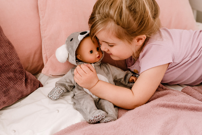 Child cuddles with baby doll in koala onesie