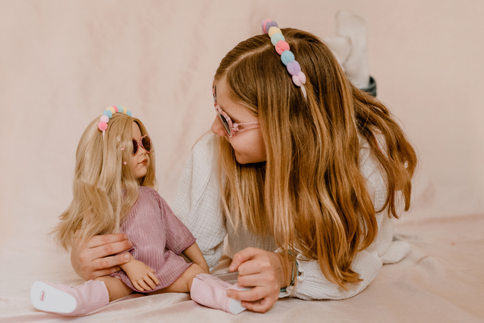 Du und Deine Puppe Goetz Kind und blonde Stehpuppe tragen im Partnerlook den gleichen Haarreif und die gleiche Sonnenbrille und schauen sich an