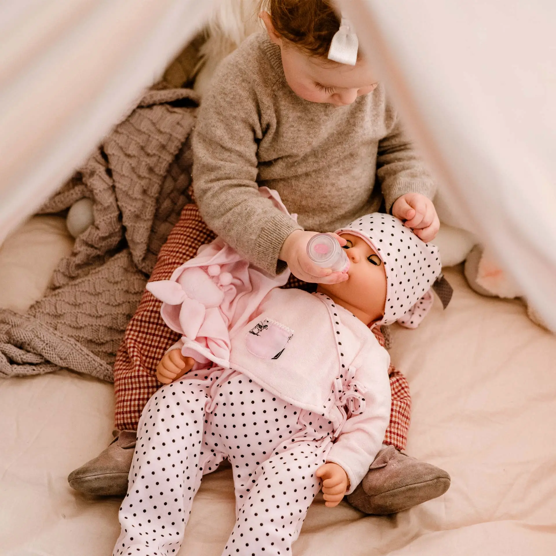 1661045 Cookie Ladies And Spots Goetz Kind spielt mit 48 cm grosser Babypuppe im rosa Anzug mit Schlafaugen und fuettert sie mit einer Flasche