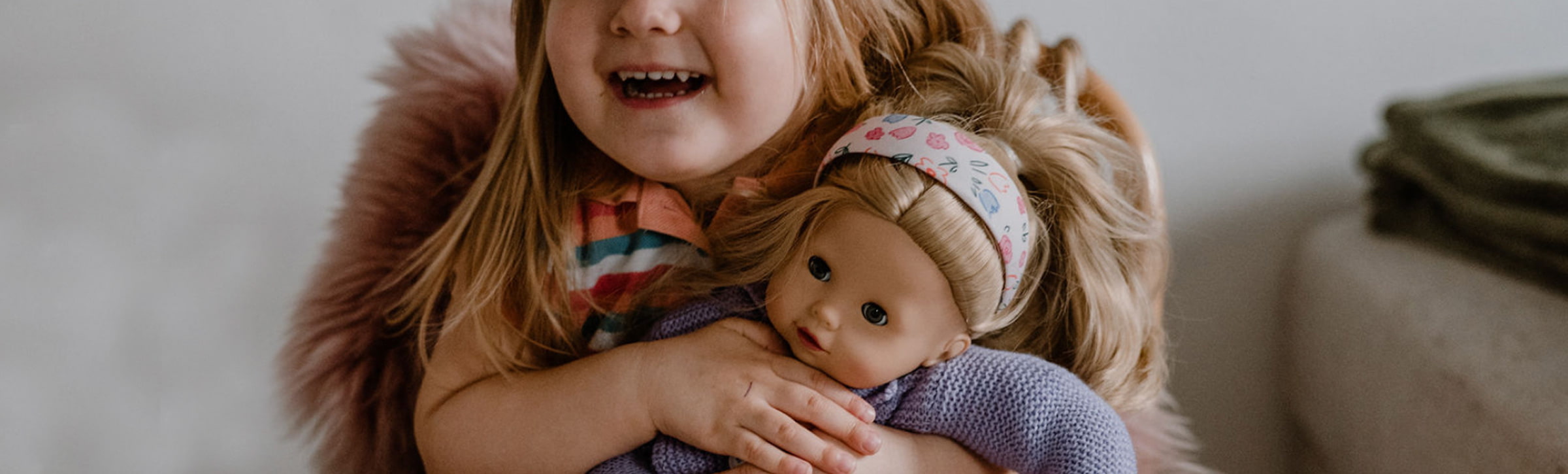Kind umarmt eine Goetz Babypuppe und laecheld in die Kamera
