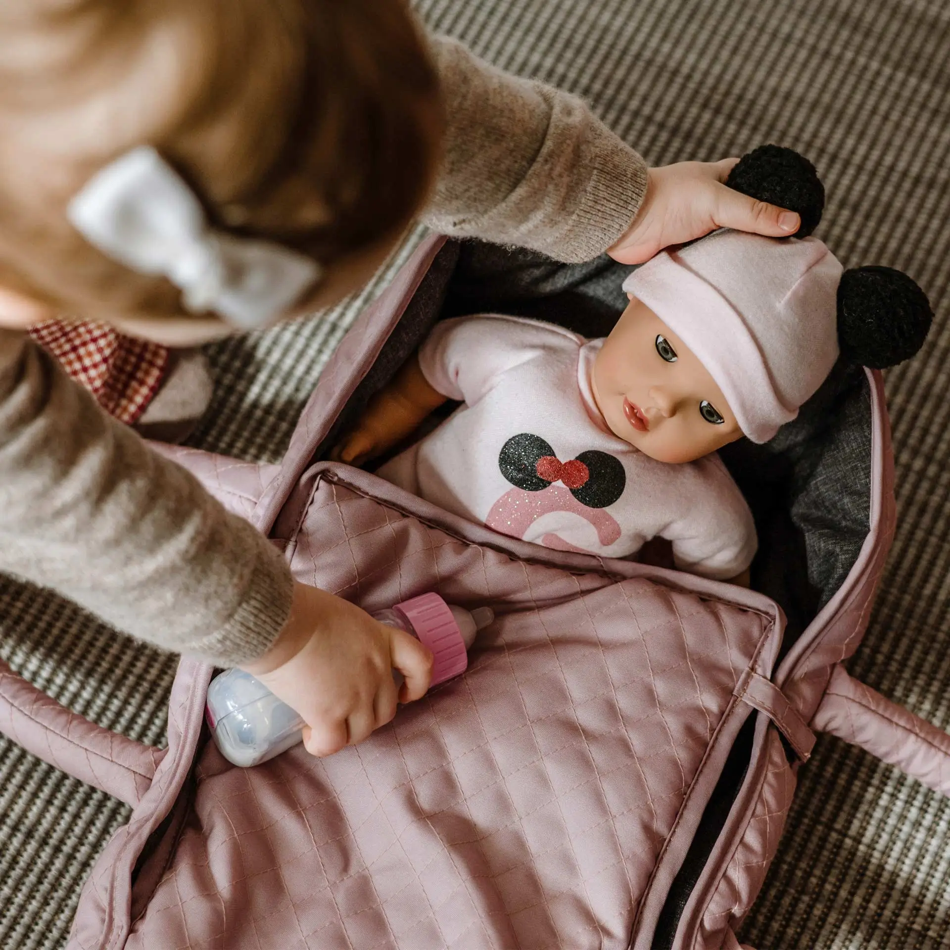 Kind spielt mit einer 33 cm großen Babypuppe mit Schlafaugen in einem rosanen Tragebettchen