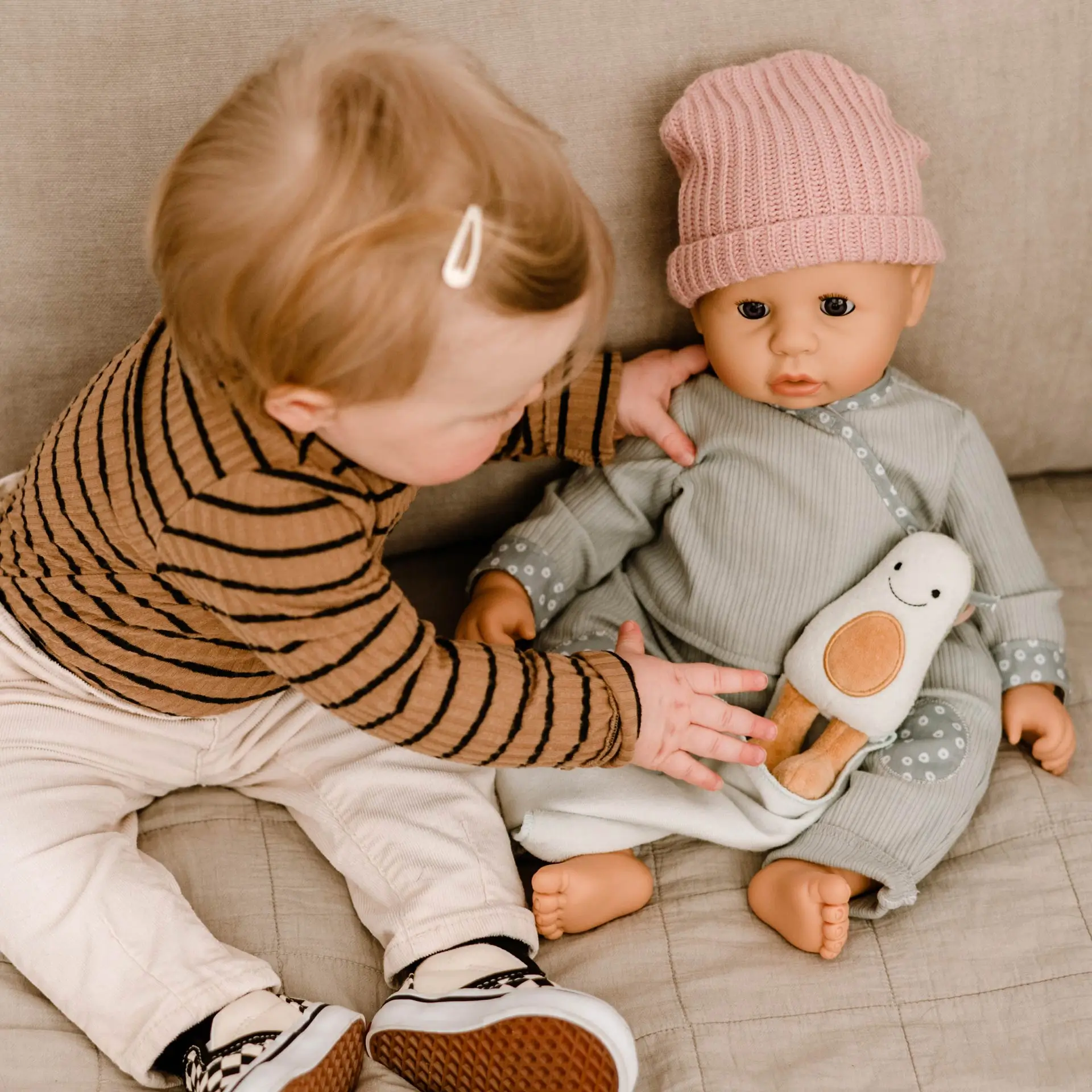 Kind sitzt neben einer 48 cm großen Babypuppe mit Schlafaugen und Avocado Stoffspielzeug