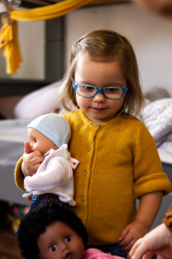 Kind haelt 33 cm grosse Babypuppe mit Muetze und Jacke in den Armen