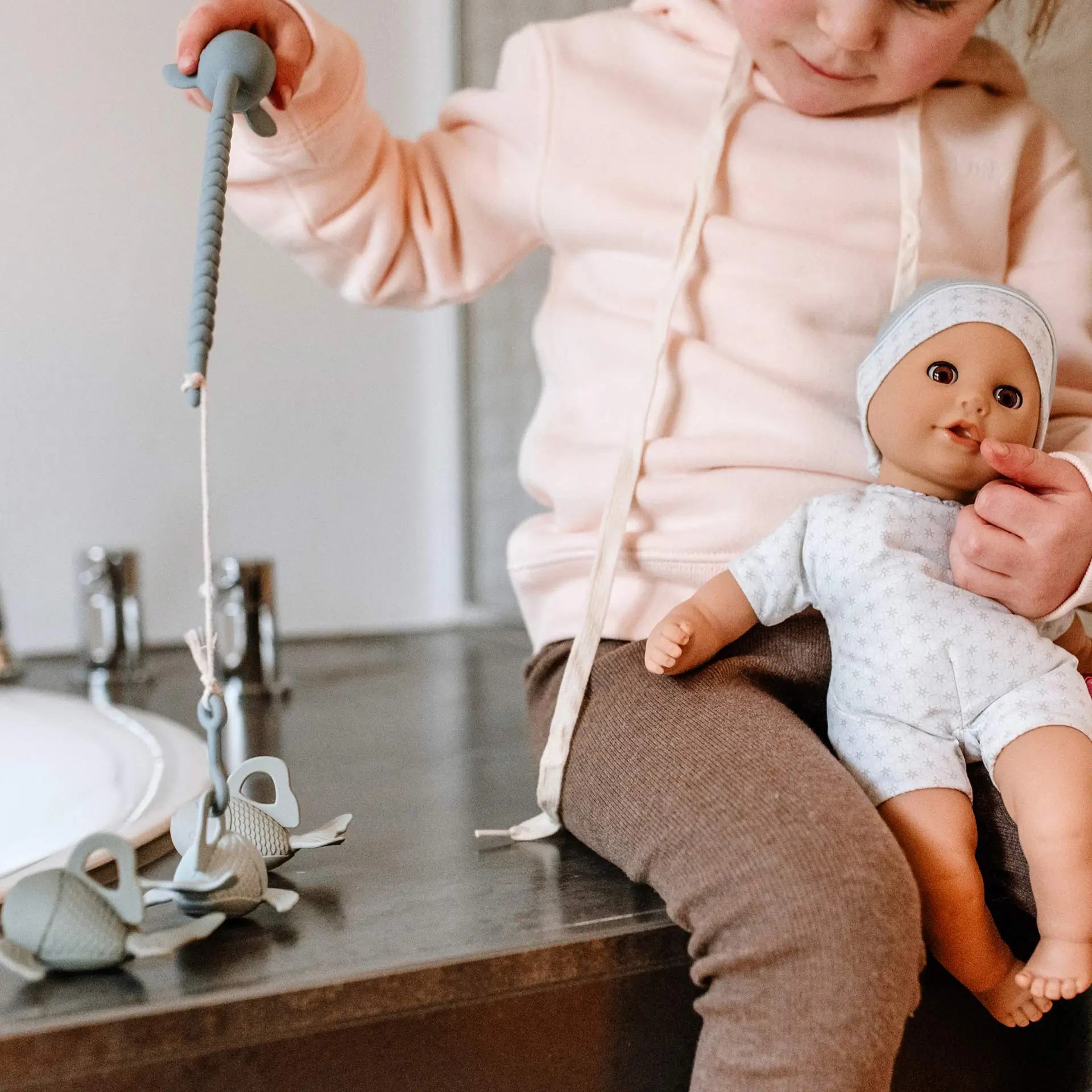 Kind spielt mit 33 cm großer Babypuppe mit Schlafaugen und Angelset mit Fischen am Waschbecken