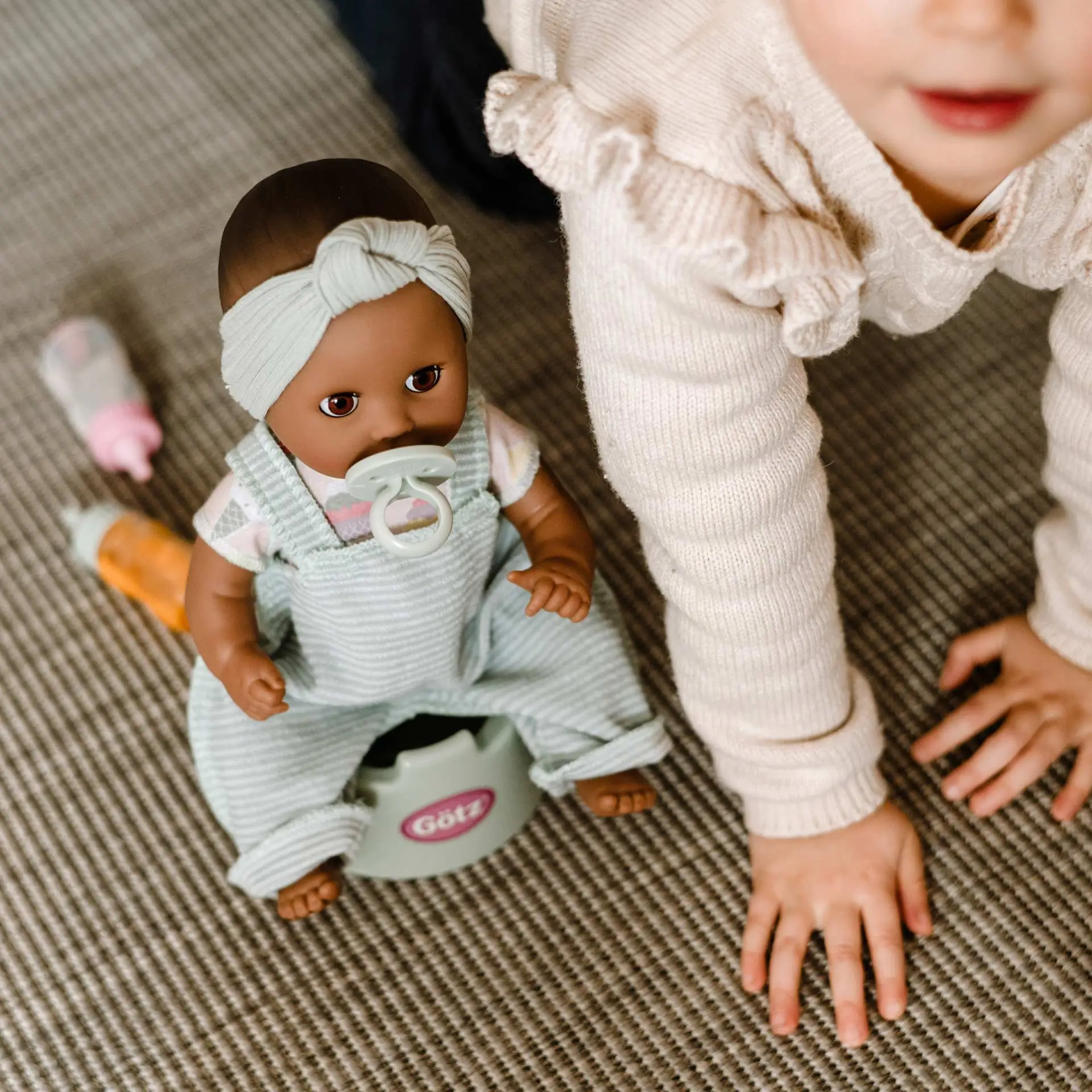 Kind sitzt auf dem Boden mit einer 33 cm grossen Babypuppe auf einem Toepfchen mit Schnuller und Schlafaugen