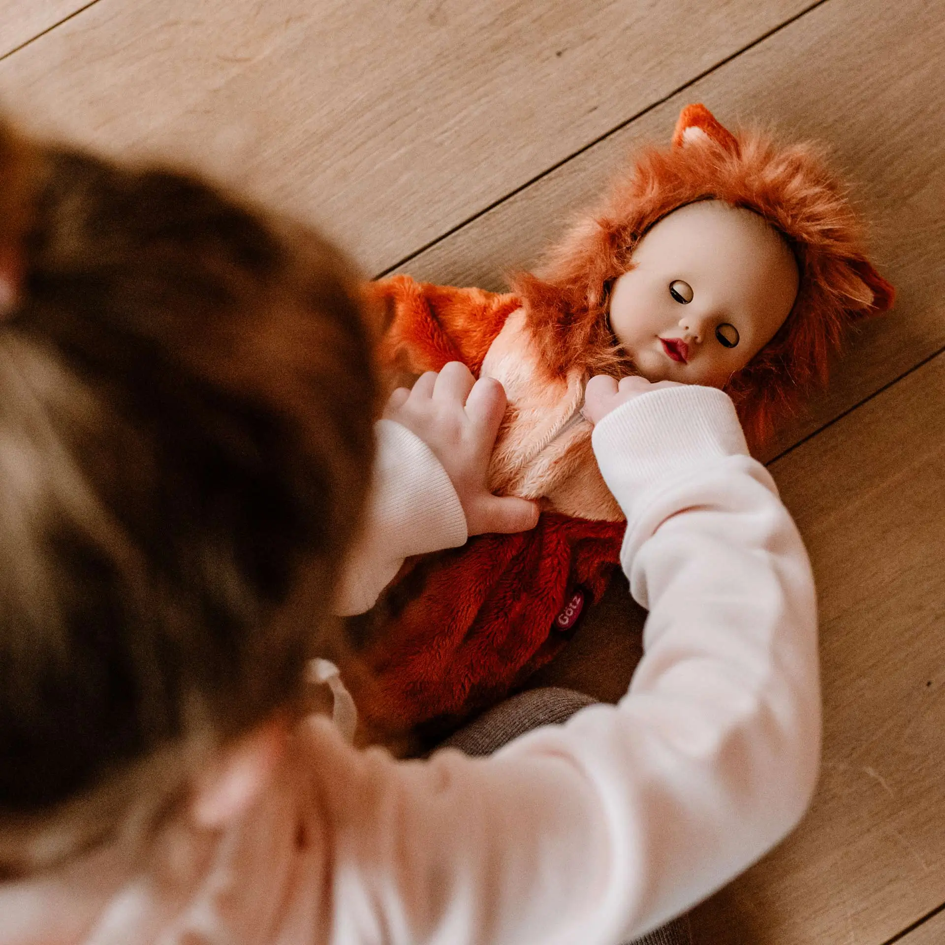 Kind zieht einer 33 cm große Babypuppe mit Schlafaugen einen Onesie im Loewendesign an