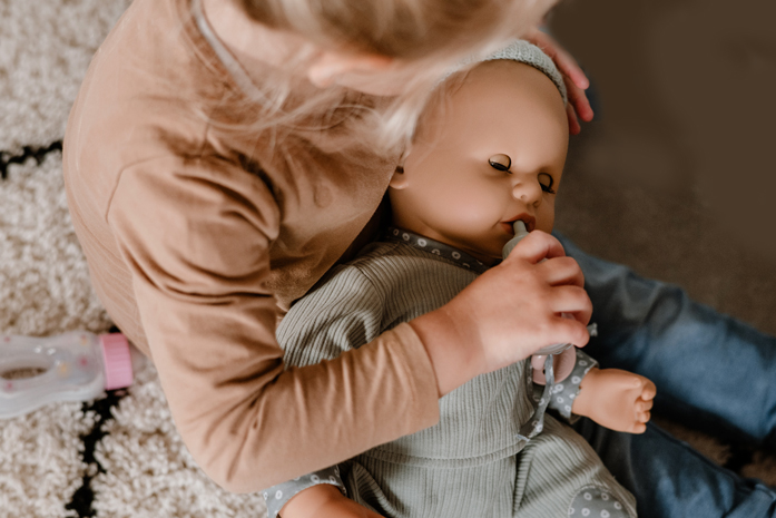 Kind fuettert Babypuppe mit Schlafaugen mit einem Flaeschchen