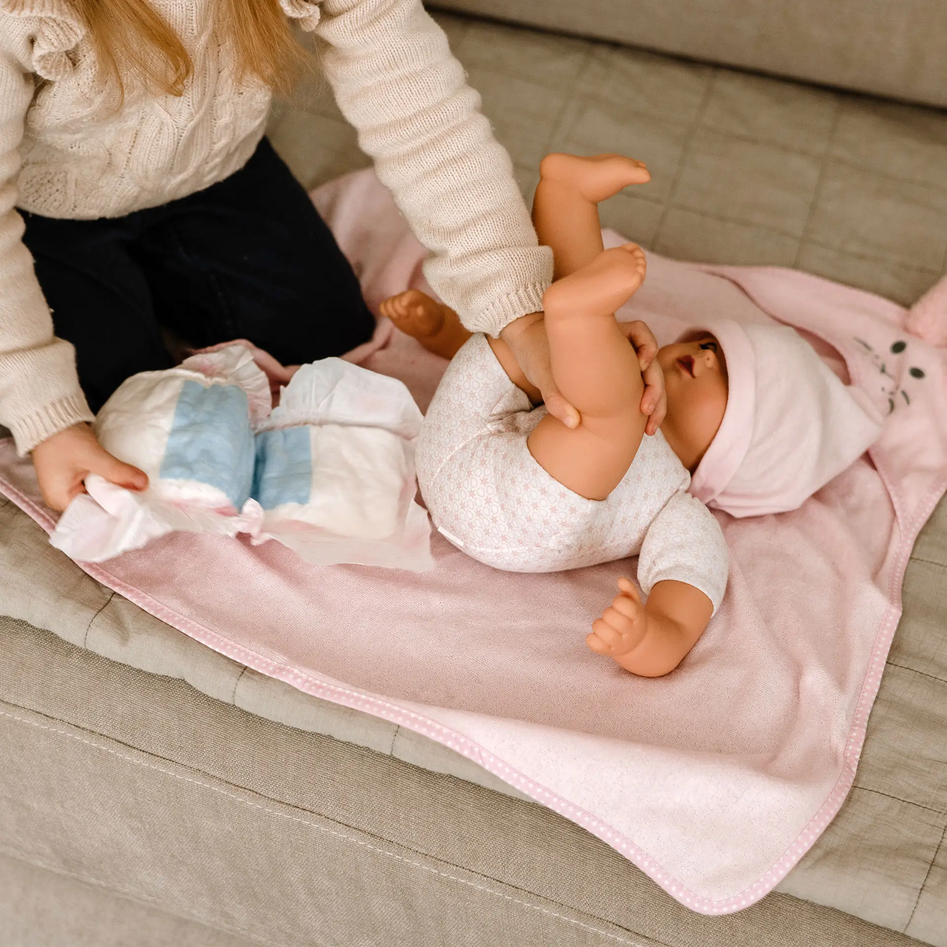 Kind wickelt eine 42 cm grosse Babypuppe auf einem rosa Badetuch