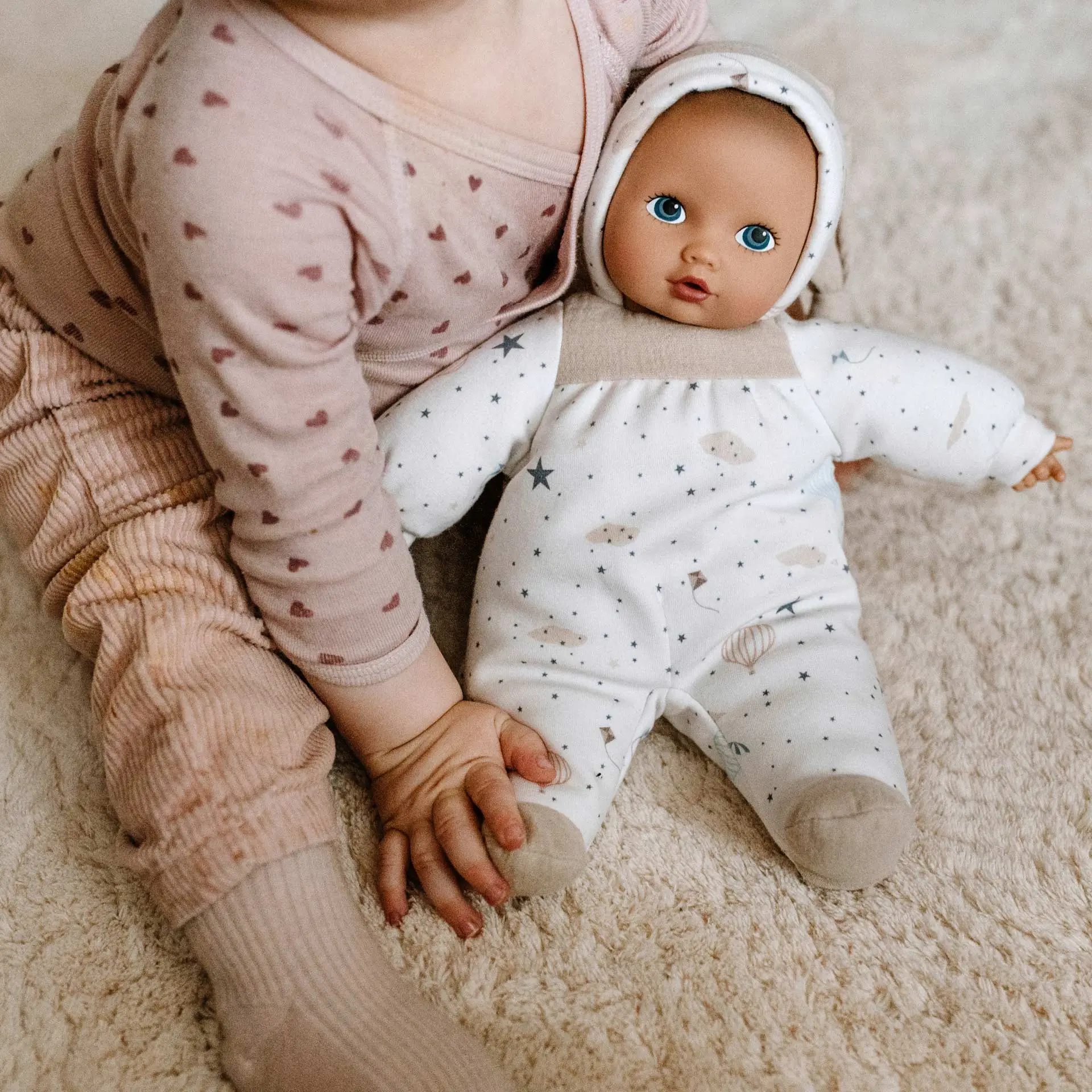2491423 Baby Pure Goetz Kind sitzt mit Erstlingspuppe im neutralen Design auf Teppich