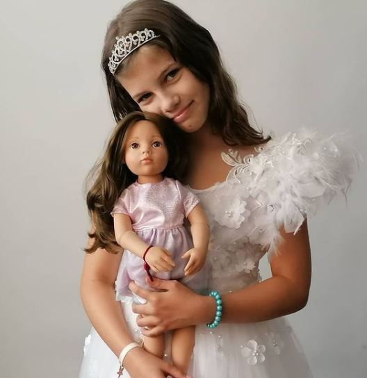 Kind umarmt eine 50 cm grosse Stehpuppe mit braunen Haaren und rosanem Kleid