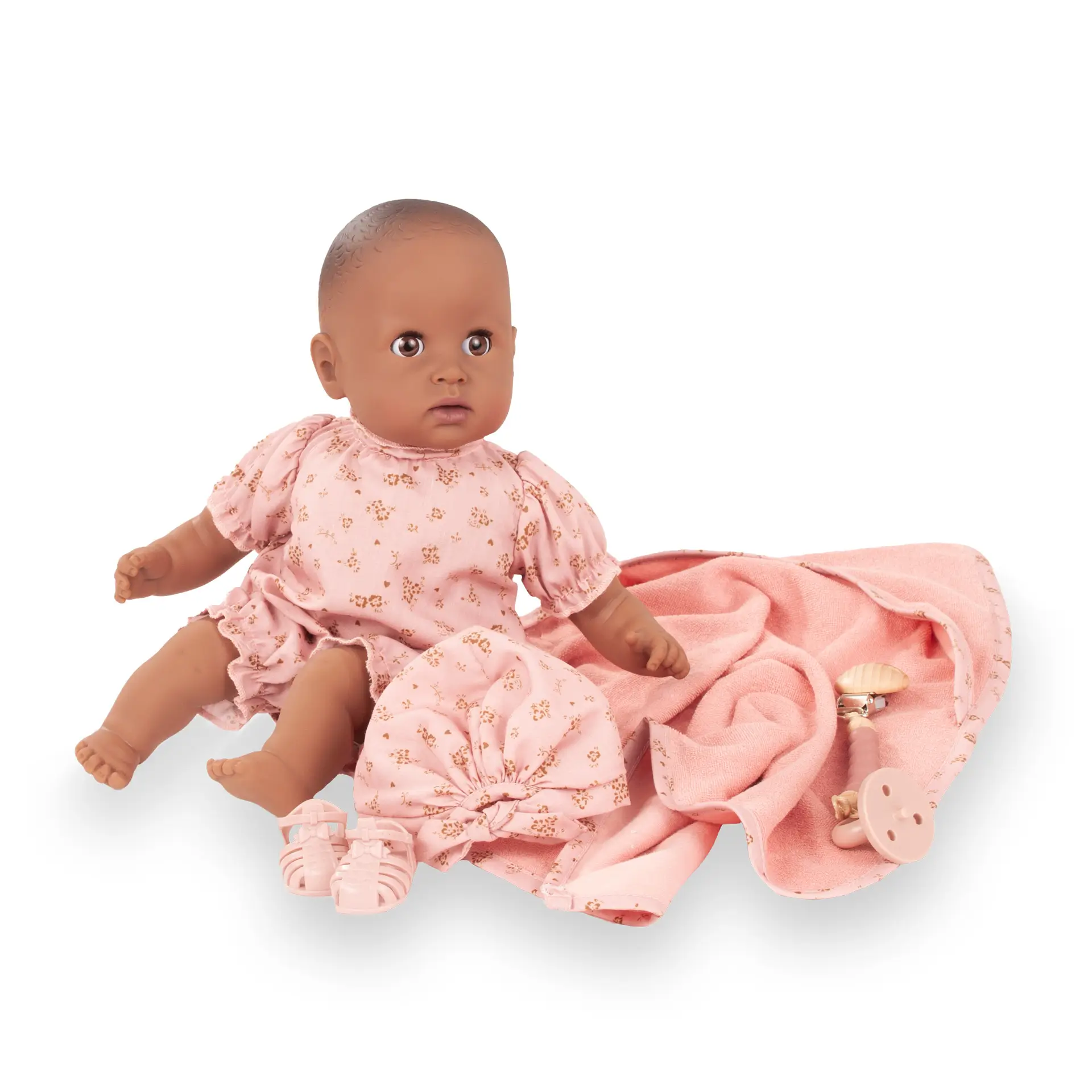 Badepuppe Gr. 33 cm in braunem Vinyl, ohne Haare mit braunen Schlafaugen. Sie traegt einen rosafarbenen Sommerstrampler mit goldenen Bluemchen und einer Muetze. Dazu ein Schnuller mit Schnullerkette, dazu ein Kapuzentuch und Badesandalen von Goetz