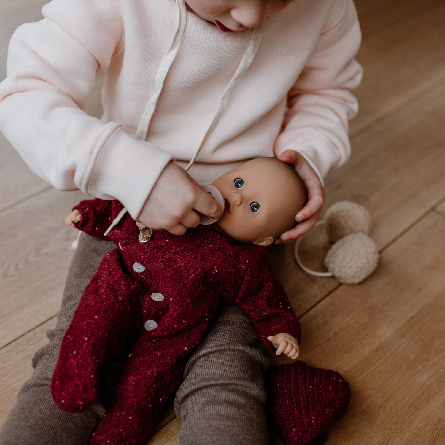 2520567 Muffin Baby Jubilee Goetz Eine 33 cm grosse Babypuppe mit Schlafaugen im roten Strampler sitzt auf dem Schoss eines Kindes
