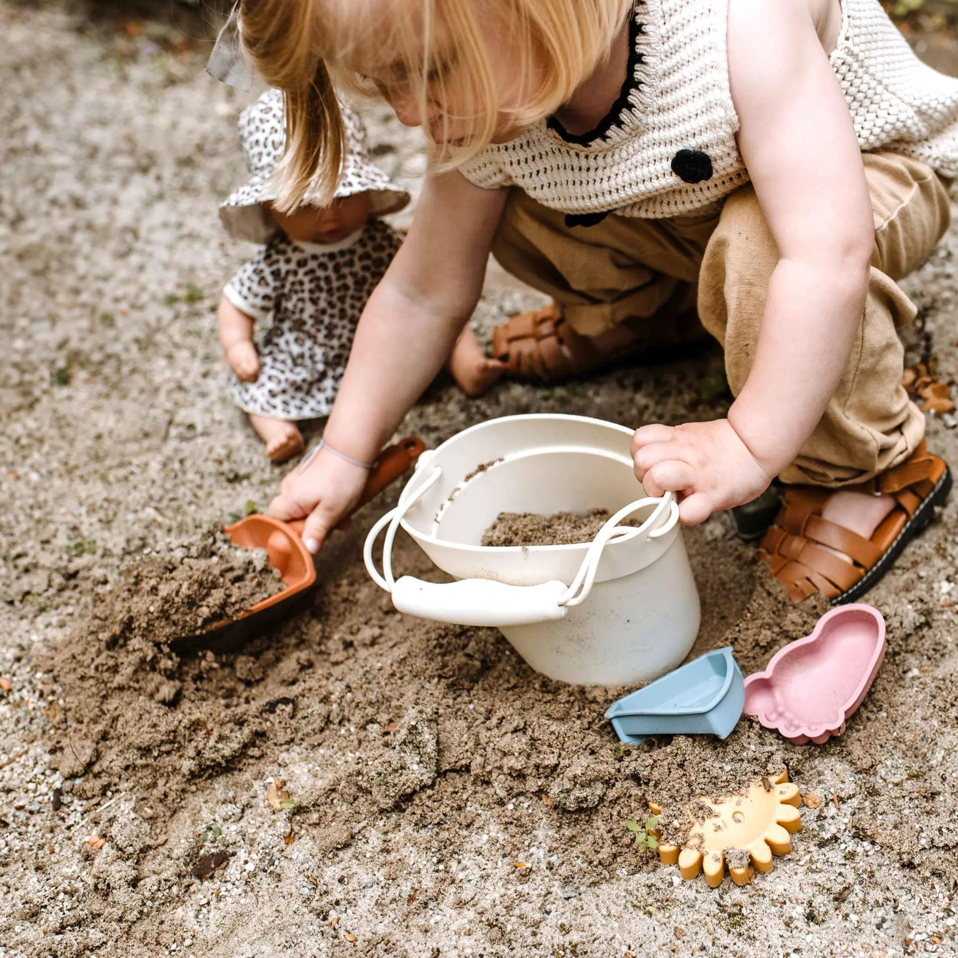 Kind spielt im Sandkasten mit Sandspielzeug und einer 33 cm grossen Babypuppe