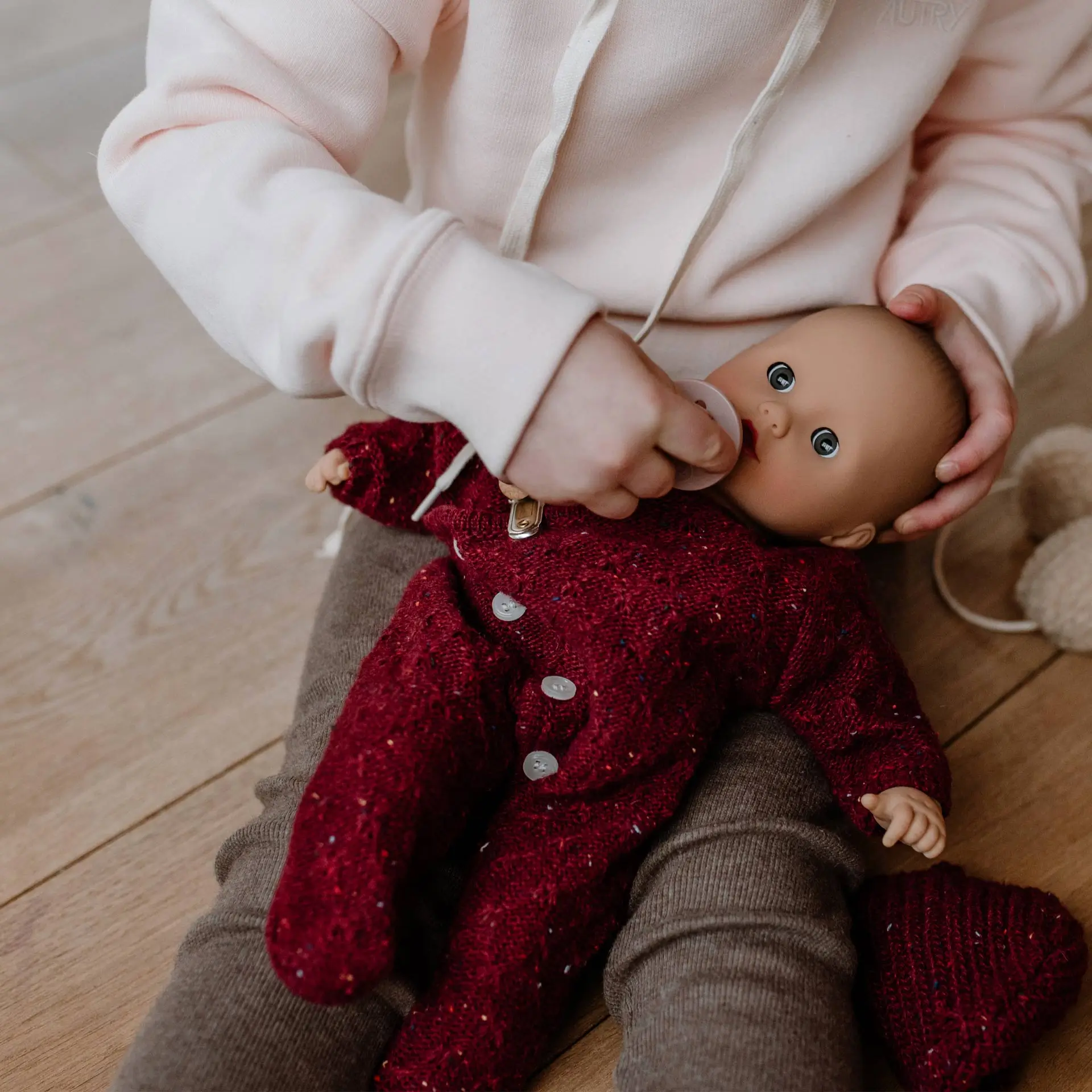 2520567 Muffin Baby Jubilee Goetz Eine 33 cm grosse Babypuppe mit Schlafaugen im roten Strampler sitzt auf dem Schoss eines Kindes