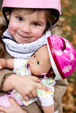 Kind  mit Helm umarmt Babypuppe mit Helm