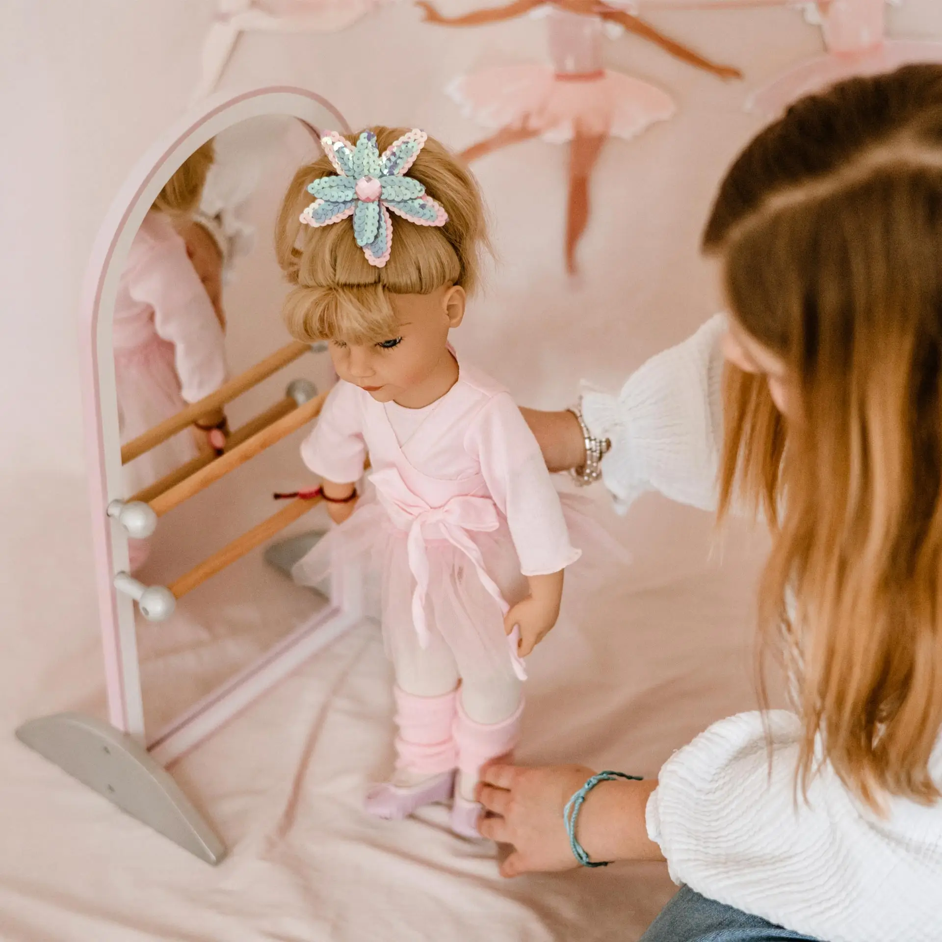 Kind spielt mit einer 50 cm großen blonden Ballerinastehpuppe an einer Ballettstange