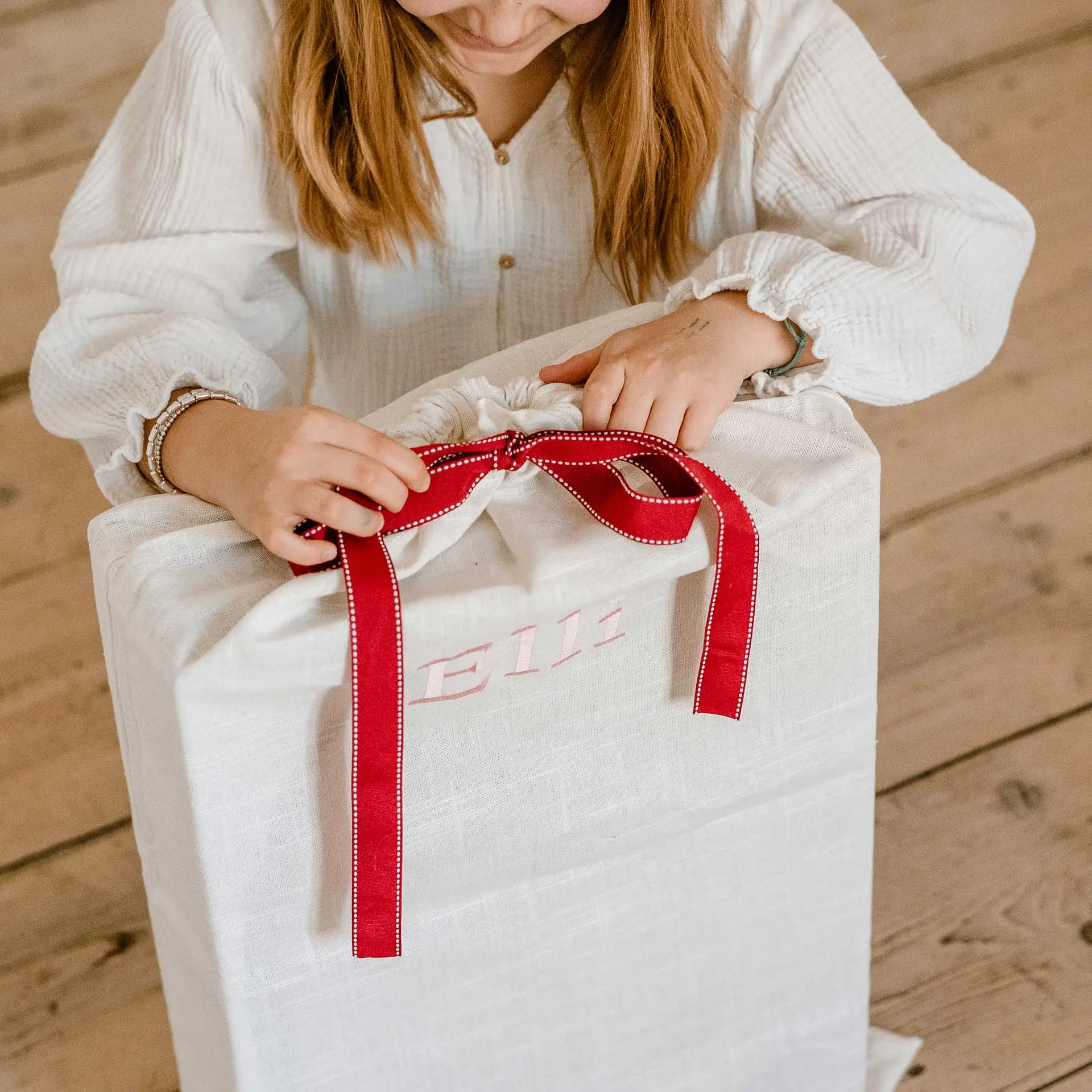 Kind oeffnet einen Leinen-Geschenkbeutel mit roter Schleife