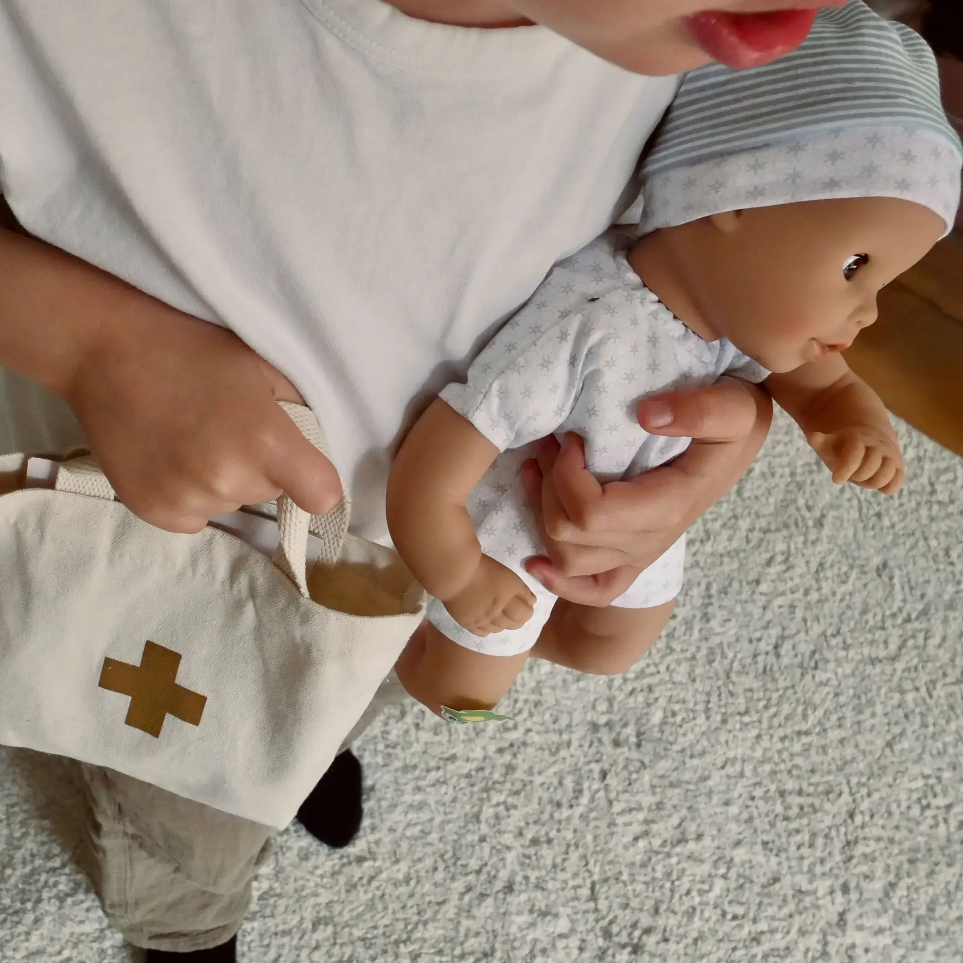 Kind traegt 33 cm grosse Babypuppe mit Weichkoerper und eine Arzttasche