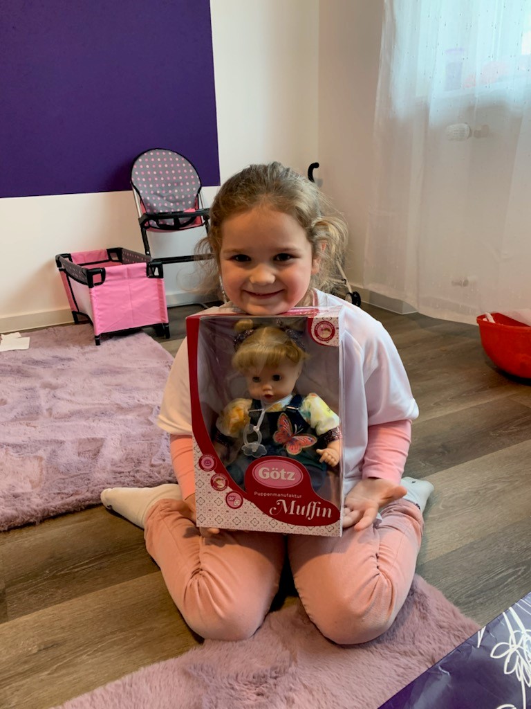 Laechelndes Kind haelt im Karton verpackte 33 cm grosse Babypuppe von Goetz in den Armen