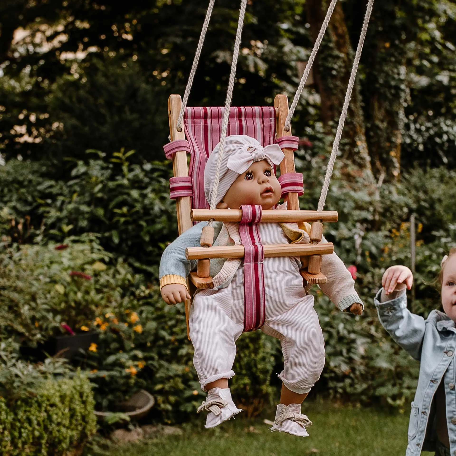 Kind schaukelt eine 48 cm große Babypuppe mit Schlafaugen in Puppenschaukel im Garten